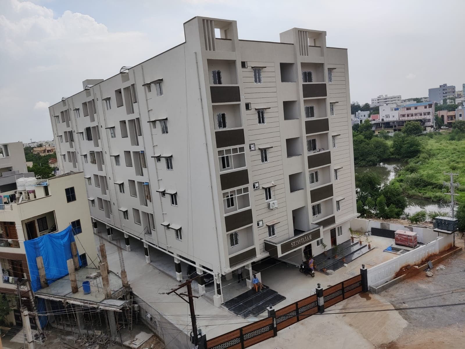 Srinivasam apartment building, fully completed and painted, with landscaped entrance and Bookings Open signage